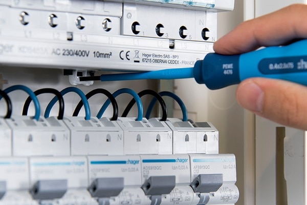 Elektriker drückt mit blauem Schraubendreher gegen Befestigungspunkt in Hager Zählerschrank