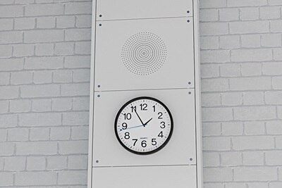 Blick in Klassenzimmer mit Fokus auf oberen Bereich der Hager Mediensäule mit analoger Uhr und Frontplatte mit Lautsprecheröffnungen