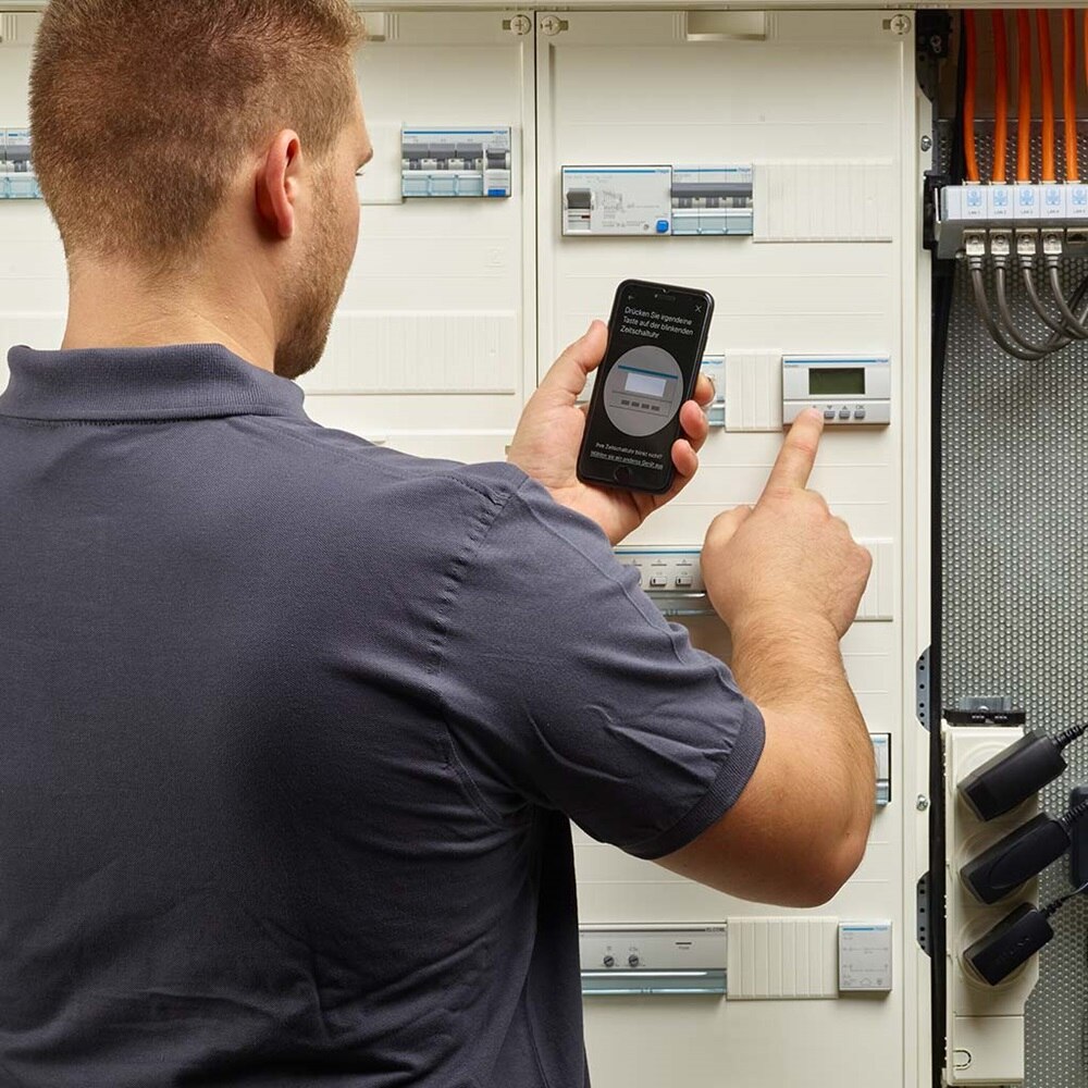 Bild vom Elektrohandwerker bei der Konfiguration der Zeitschaltuhr per Bluetooth am Smartphone.