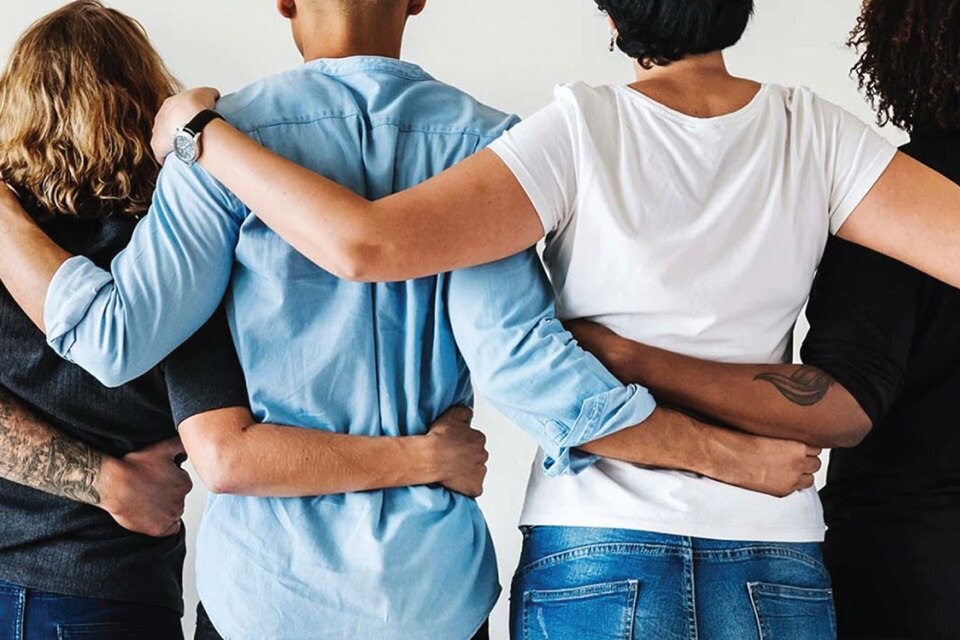 Group of people standing back to camera with linked arms promoting teamwork and unity