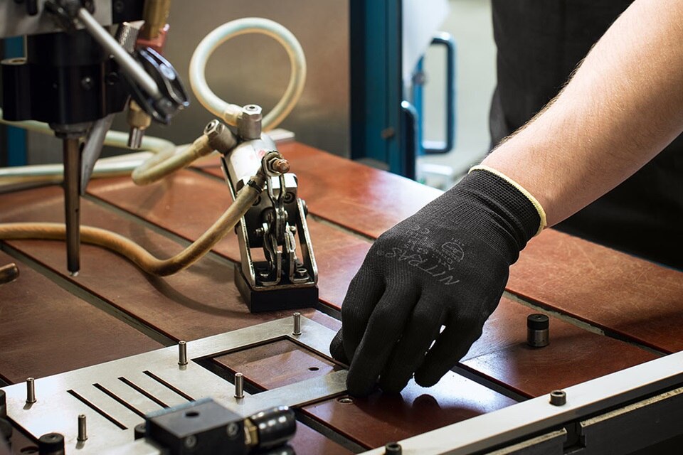 Hand eines Arbeiters mit Sicherheitshandschuh beim Einstellen von Geräten in einer industriellen Automatisierungsumgebung