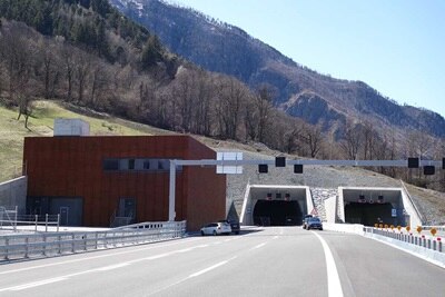 Straße, die an einem sonnigen Tag zu einem Zwillings-Tunnel-Eingang mit Verkehrsmanagementsystem führt