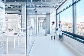 Modernes Laborinterieur mit zwei Fachkräften, die am Fenster diskutieren, mit Kabeltrassen und elektrischen Installationen