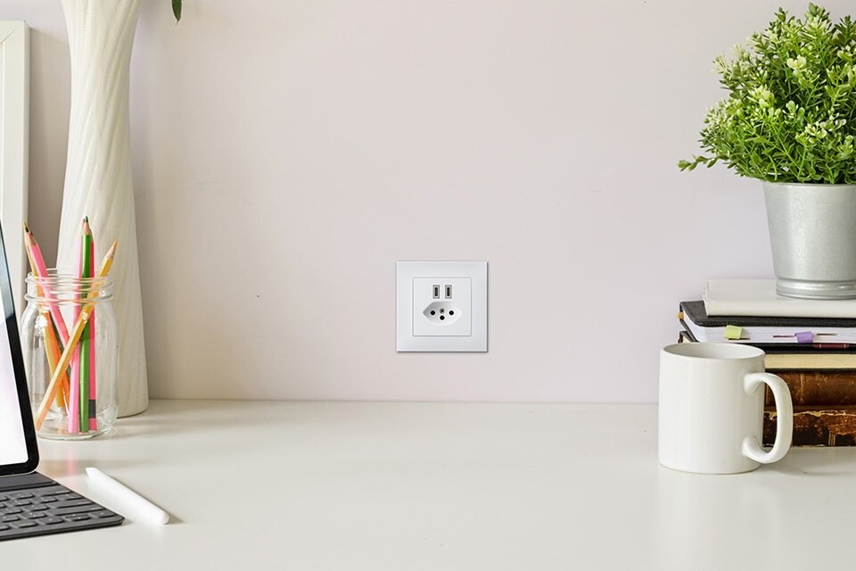 Modernes Büro mit weißer Wandsteckdose, Schreibtischaccessoires und Pflanze