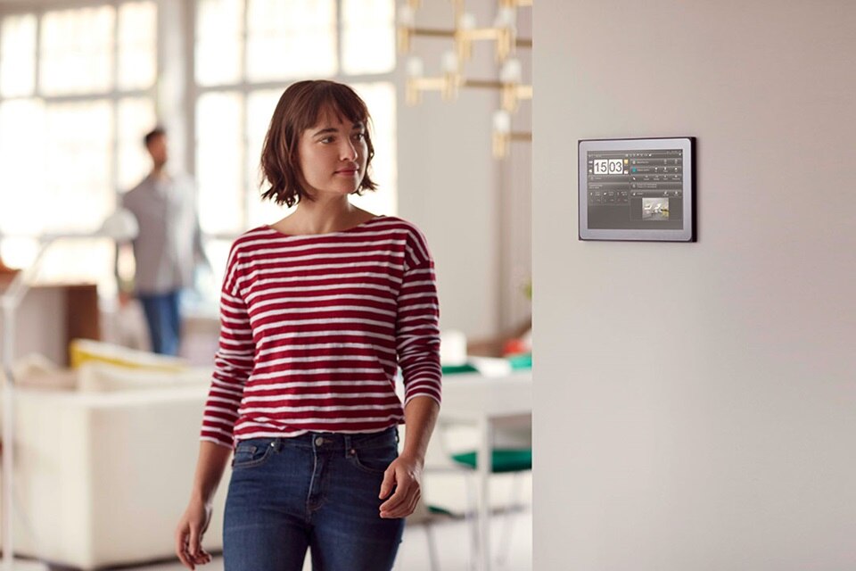 Person steht in einem modernen Wohnraum mit einem Smart-Home-Steuerungspanel an der Wand