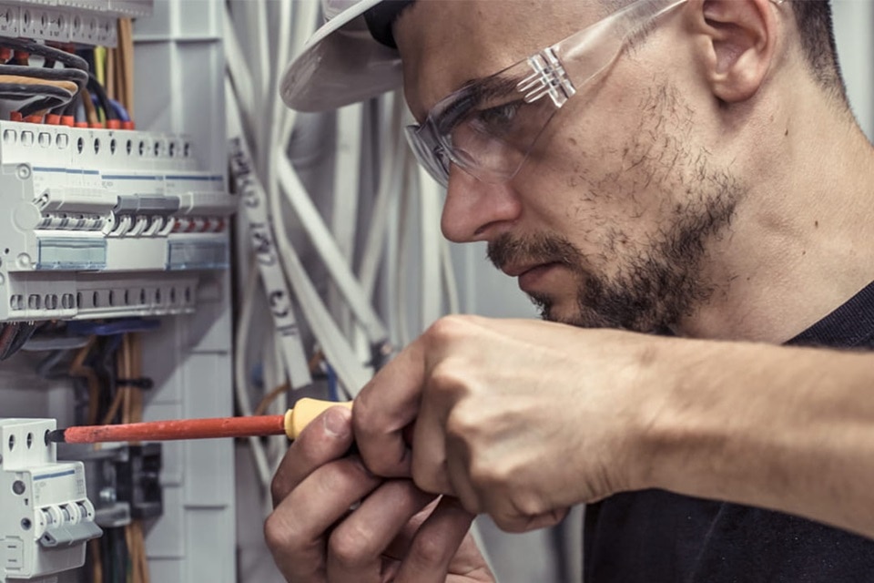 Techniker arbeitet mit Schutzbrille und isoliertem Schraubendreher an einem Elektroverteilungskasten