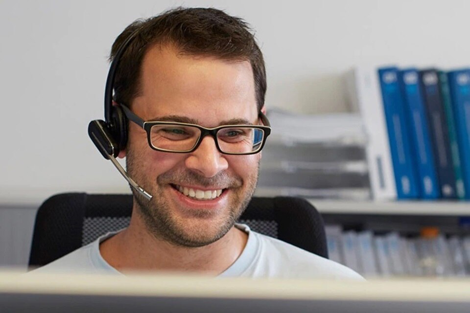 Lächelnde Person mit Headset arbeitet in einer Büroumgebung