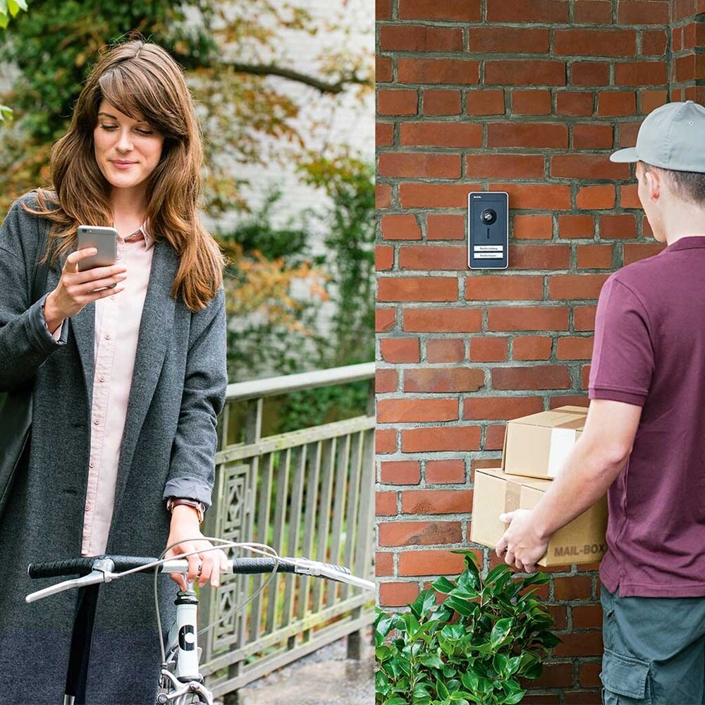 Eine Frau öffnet dem Postboten von unterwegs über das Handy die Tür.