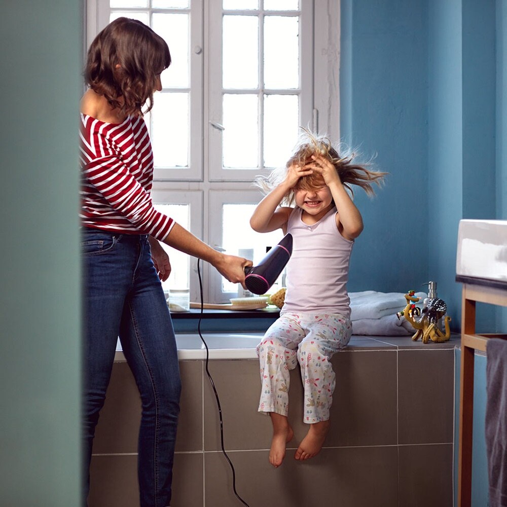 Eine Mutter föhnt ihr Kind im Badezimmer.