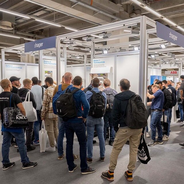 Besucher am Messestand von Hager auf einer Industriemesse, die mit Ausstellungen und Unternehmensvertretern interagieren.
