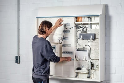 Techniker überprüft einen großen Elektroverteiler mit verschiedenen Leitungsschutzschaltern und Verkabelungen