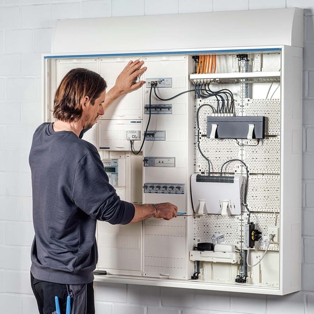 Techniker überprüft einen großen Elektroverteiler mit verschiedenen Leitungsschutzschaltern und Verkabelungen