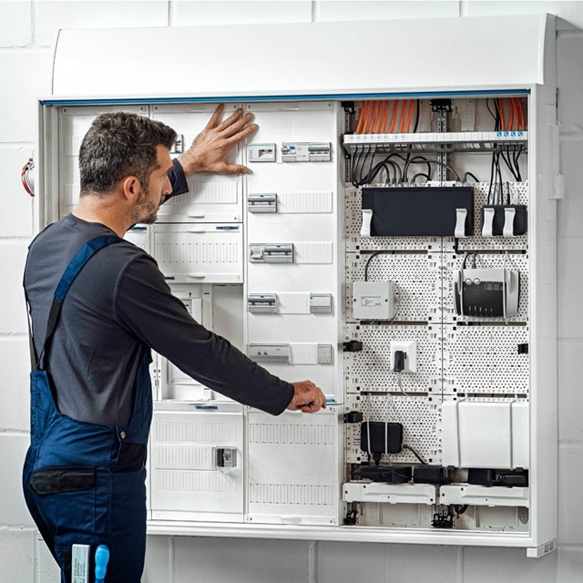 Techniker überprüft einen großen Elektroverteiler mit verschiedenen Leitungsschutzschaltern und Verkabelungen