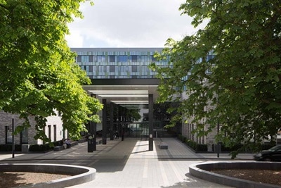 Eingang eines modernen Bürogebäudes mit Glasfassade und grünen Bäumen