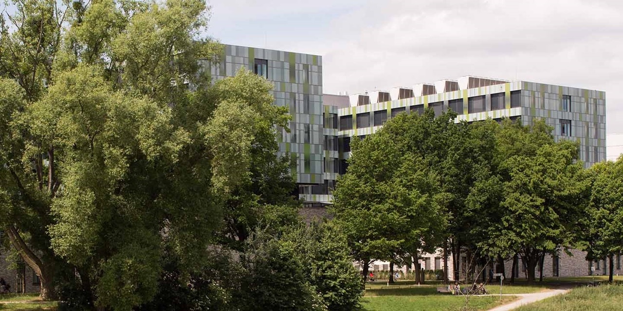 Modernes Bürogebäude mit reflektierender Glasfassade umgeben von grünen Bäumen