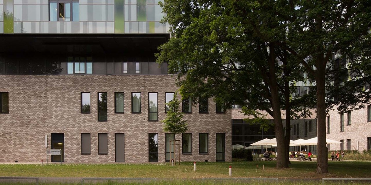 Moderne Gewerbegebäudefassade mit großen Fenstern und Außenbereich mit Sitzgelegenheiten unter Bäumen