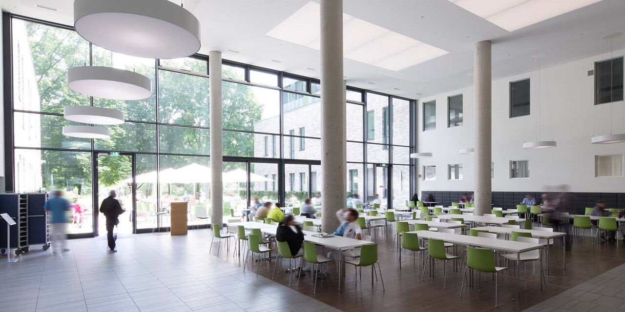 Modernes Cafeteria-Interieur mit Personen, großen Fenstern und hängenden runden Beleuchtungskörpern