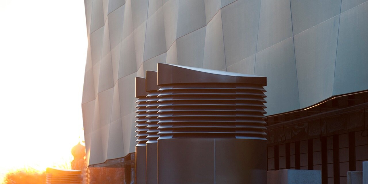 Moderne Architekturdetails mit geometrischer Metallverkleidung und Lüftungssystem vor einem Himmel bei Sonnenuntergang
