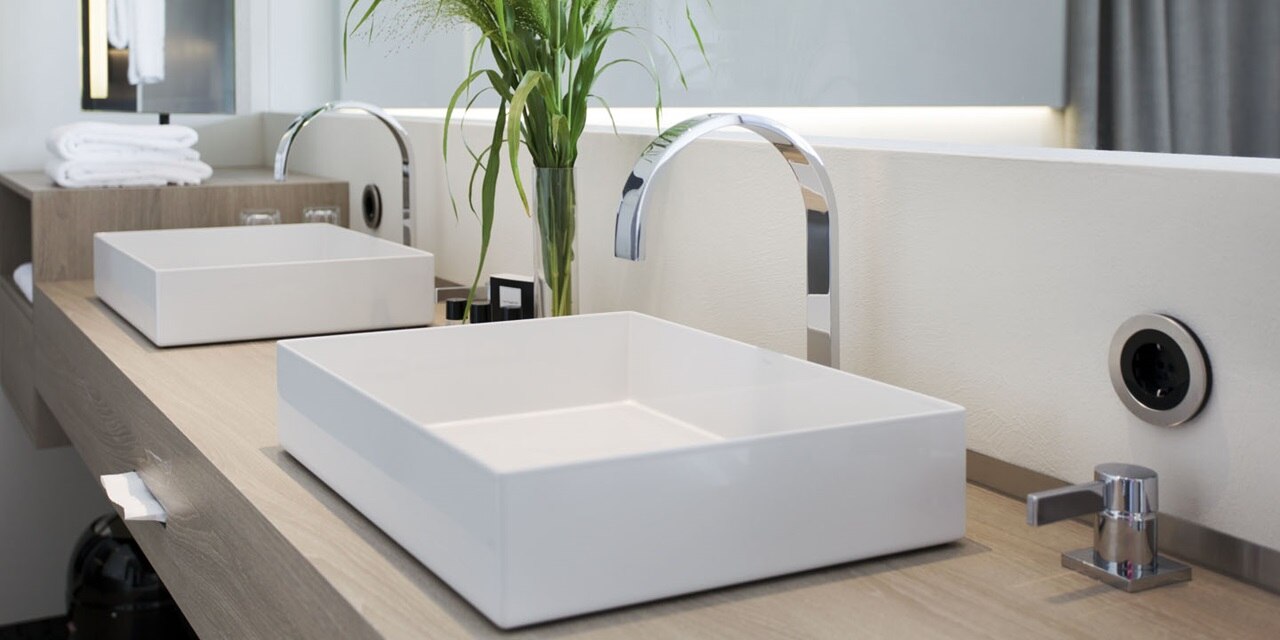 Modernes Badezimmer-Interieur mit weißen quadratischen Becken, Chromarmatur und Wandsteckdose