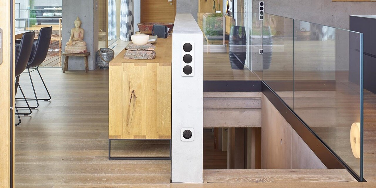 Modernes Wohndesign mit einer Betonsäule mit integrierten Steckdosen und Schaltern, Glasgeländer für die Treppe