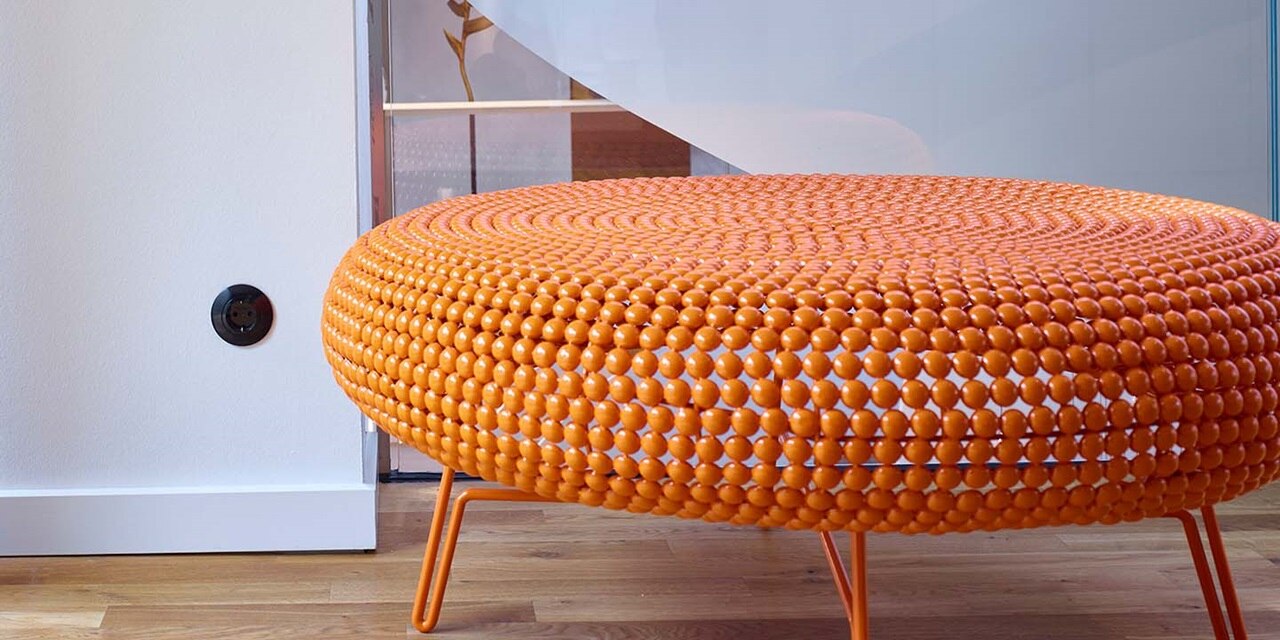 Oranger runder Ottoman in der Nähe einer schwarzen Wandsteckdose in einem modernen Interieur