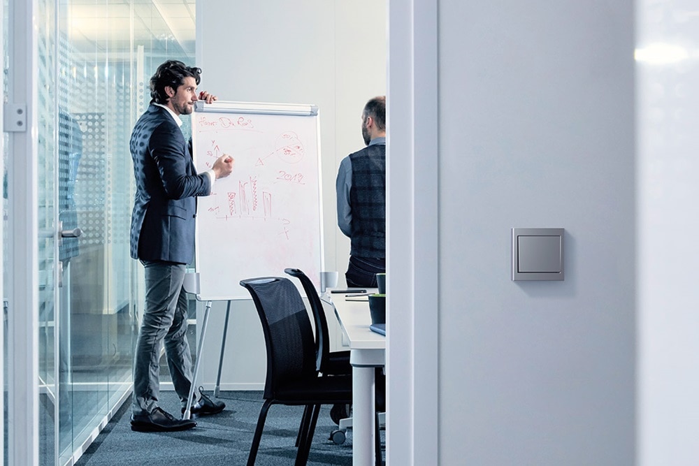 Berker Lichtschalter, im Hintergrund eine Besprechung in einem Sitzungsraum