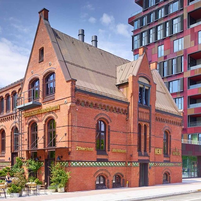 Traditionelles rotes Backsteingebäude neben einem modernen Wohnkomplex unter klarem Himmel