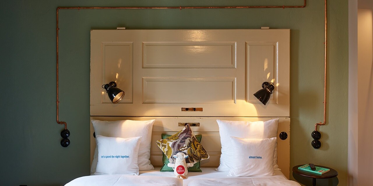 Stilvolles Schlafzimmer-Interieur mit sichtbaren Kupferrohren und schwarzen Wandleuchten über einem Doppelbett mit Dekokissen