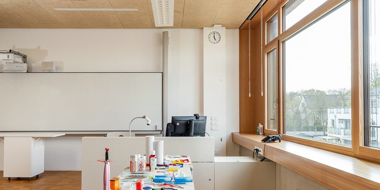 Modernes Bürointerieur mit weißen Wänden, einem großen Fenster, Holzdetails und verschiedenen Bürogeräten, einschließlich einer Uhr und elektrischen Steckdosen an der Wand