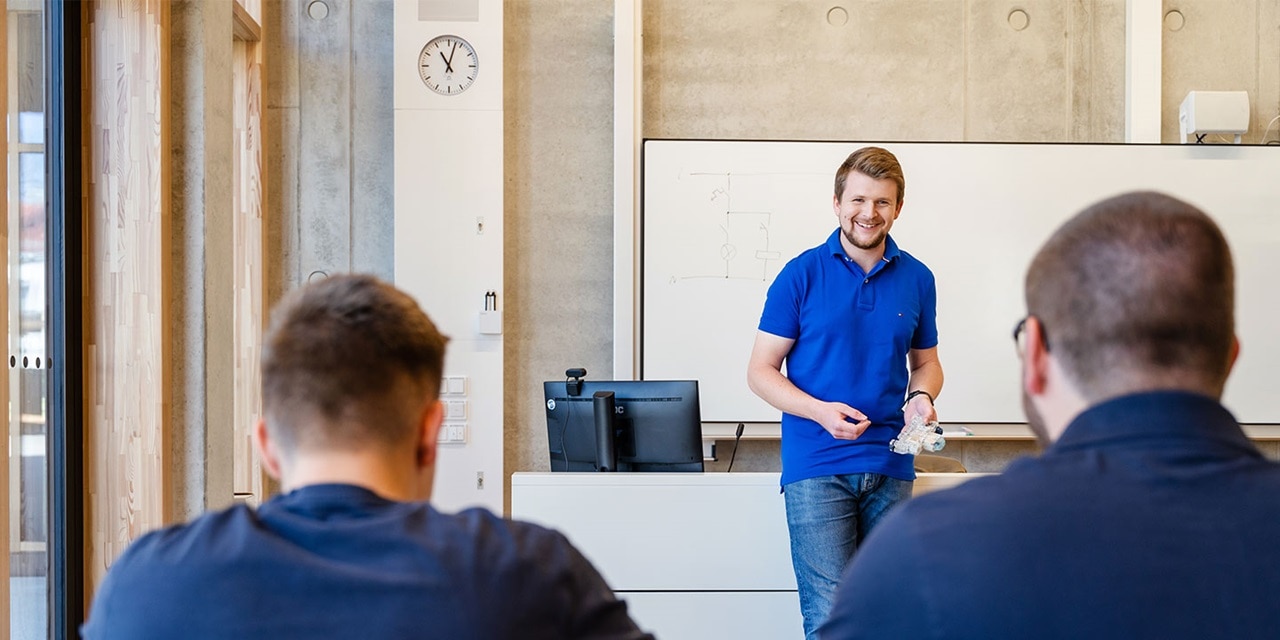 Berufliche Schulungssitzung mit einem lächelnden Präsentator vor einem Whiteboard und aufmerksamen Teilnehmern, die dem Präsentator gegenüber sitzen