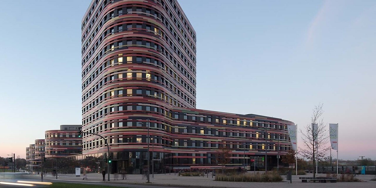 Moderne geschwungene Architektur eines mehrstöckigen Gebäudes mit beleuchteten Fenstern in der Abenddämmerung