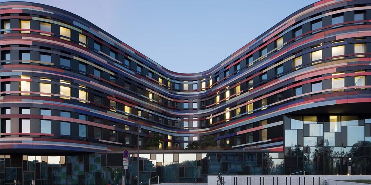 Modernes, geschwungenes Bürogebäude mit reflektierenden Fenstern und farbenfroher Fassade in der Abenddämmerung