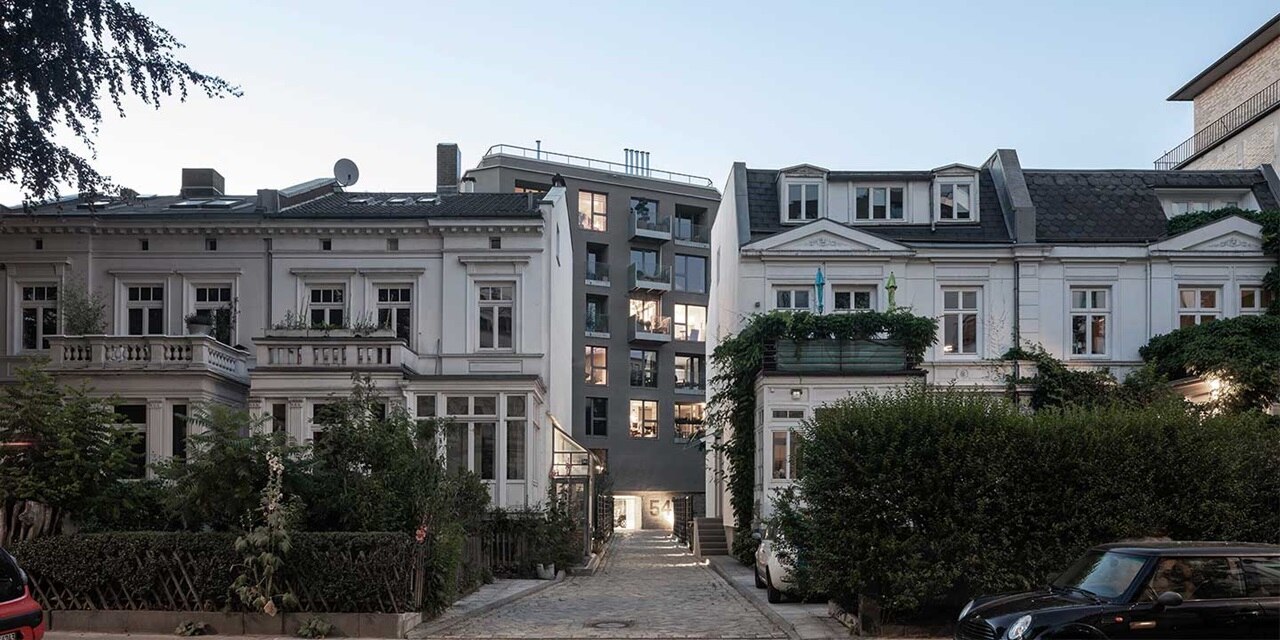 Modernes Apartmentgebäude eingebettet zwischen traditionellen Häusern mit Grünanlagen in der Abenddämmerung