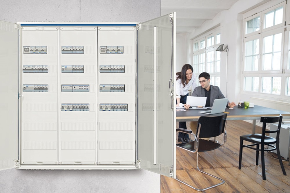 Hager Feldverteiler, im Hintergrund arbeiten eine Frau und ein Mann im Büro