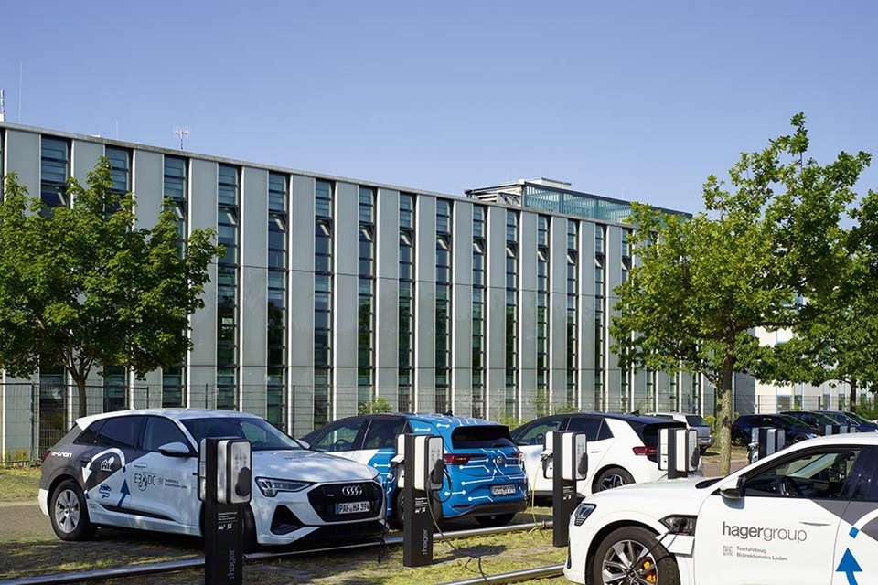 Elektrofahrzeuge der Hager Group an einer Ladestation vor einem modernen Bürogebäude beim Aufladen
