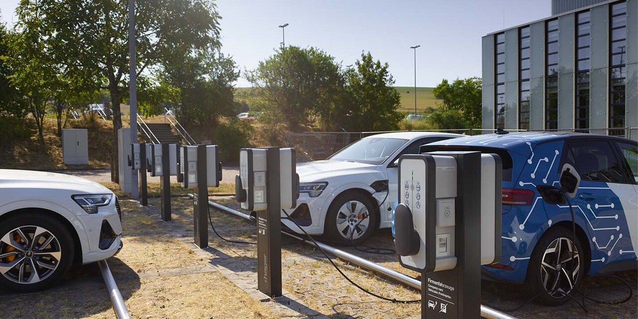Elektrofahrzeuge werden an Aufladestationen im Freien geladen, mit moderner Architektur im Hintergrund