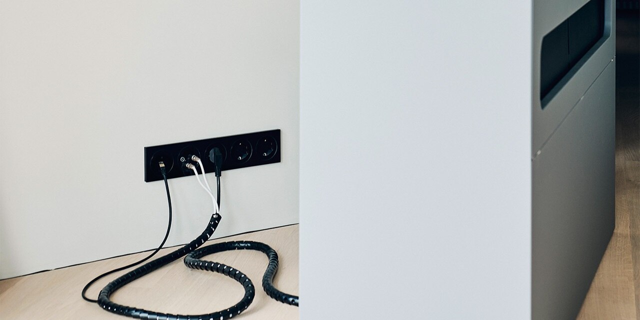 Moderne schwarze Wandsteckdosenleiste mit mehreren eingesteckten Kabeln an einer hellfarbigen Wand neben einem Küchenschrank