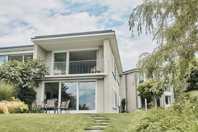 Modernes zweistöckiges Haus mit großen Fenstern und Balkon, gestalteter Garten im Vordergrund