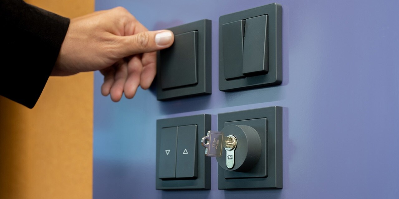 Hand nähert sich modernen schwarzen Lichtschaltern und Schlüsselschalter an farbiger Wand