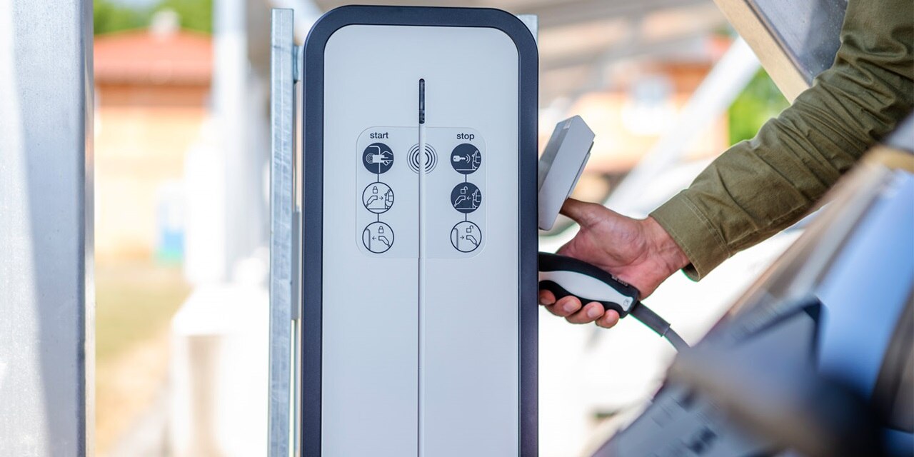 Ladestation für Elektrofahrzeuge mit Bedienungsanleitung und Person, die einen Ladestecker hält