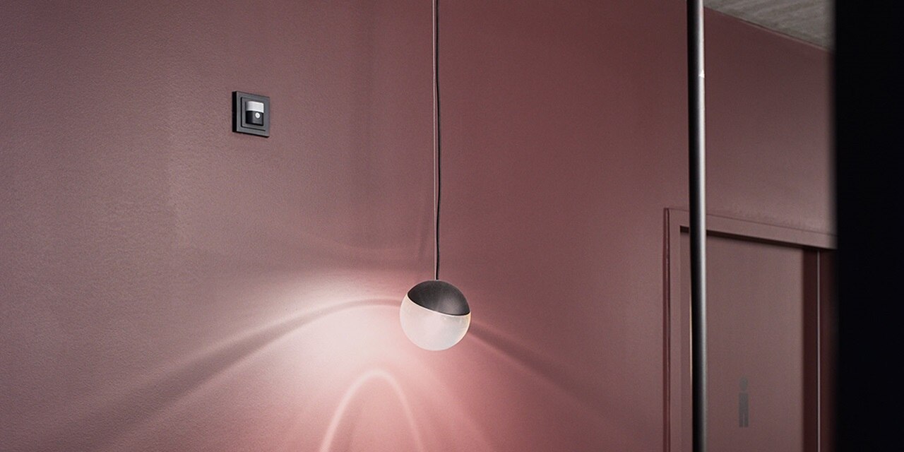 Modernes Interieur mit Hängelampe und Designer-Lichtschalter an einer mauvefarbenen Wand