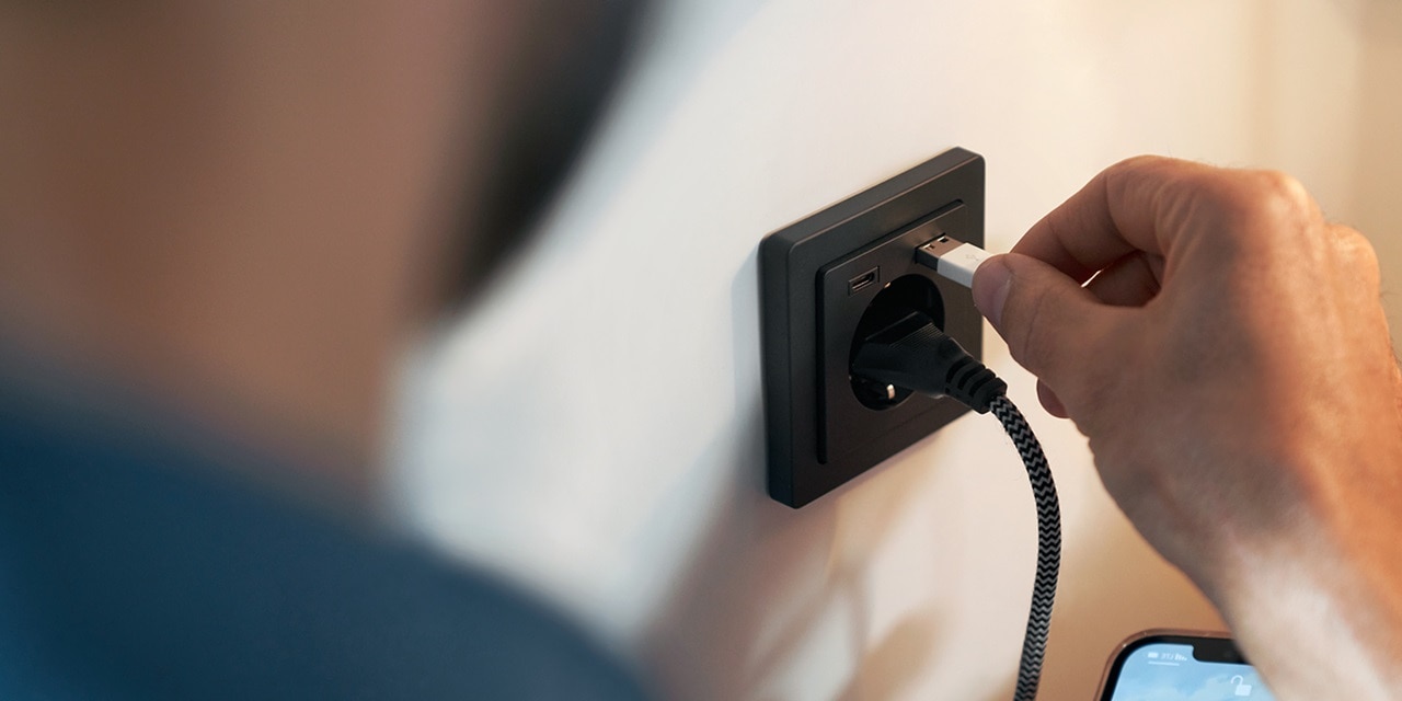Person steckt USB-Kabel in eine moderne, wandmontierte USB-Steckdose neben einer Stromsteckdose