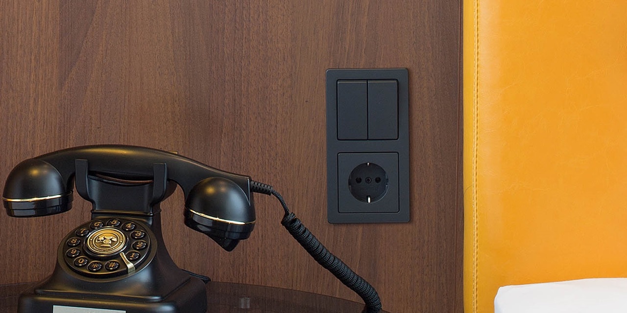 Retro schwarzes Telefon auf einem Schreibtisch mit moderner Steckdose und Schaltern an einer Holzwand