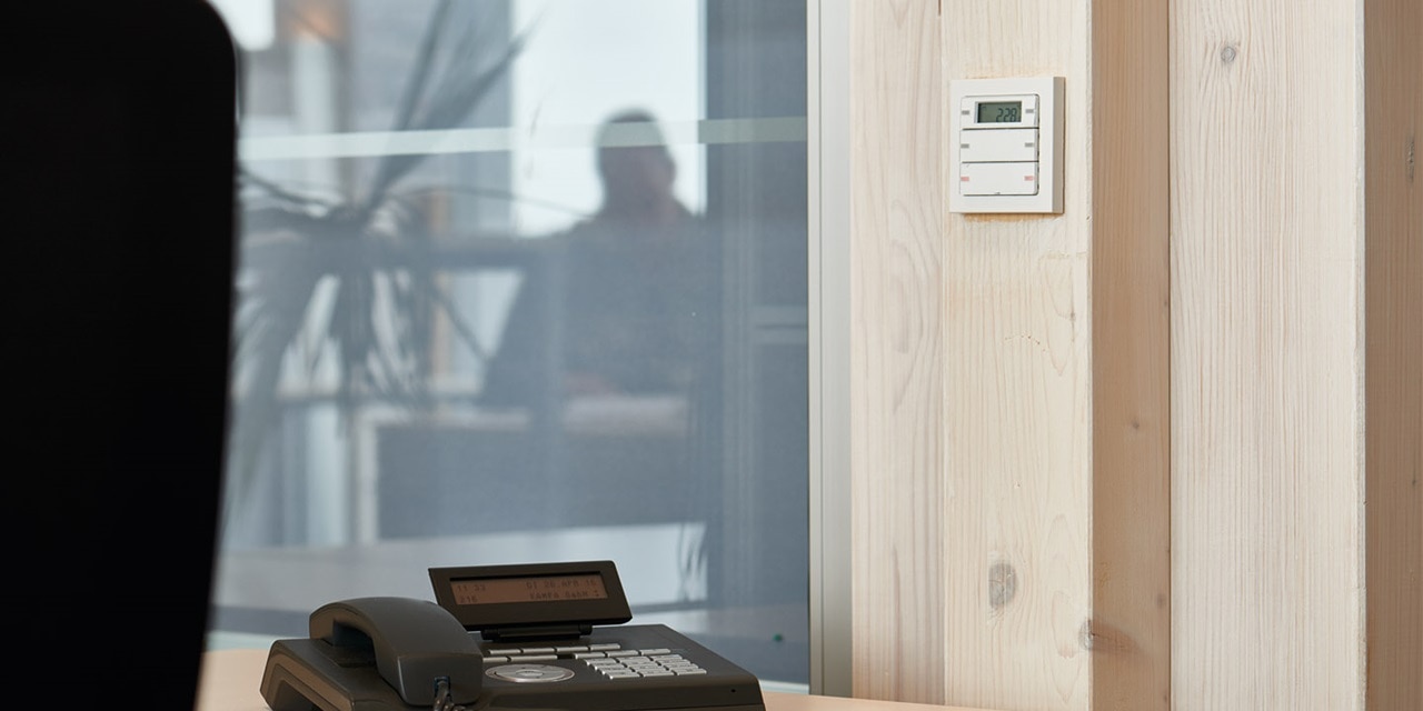 Modernes Büroumfeld mit programmierbarem Wandthermostat und einem Schreibtischtelefon im Vordergrund