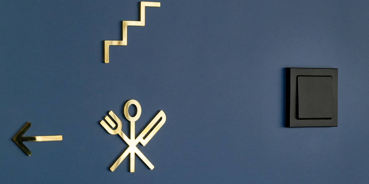 Moderner schwarzer Lichtschalter an blauer Wand mit dekorativen goldenen Symbolen für Energie, Essen und Richtung