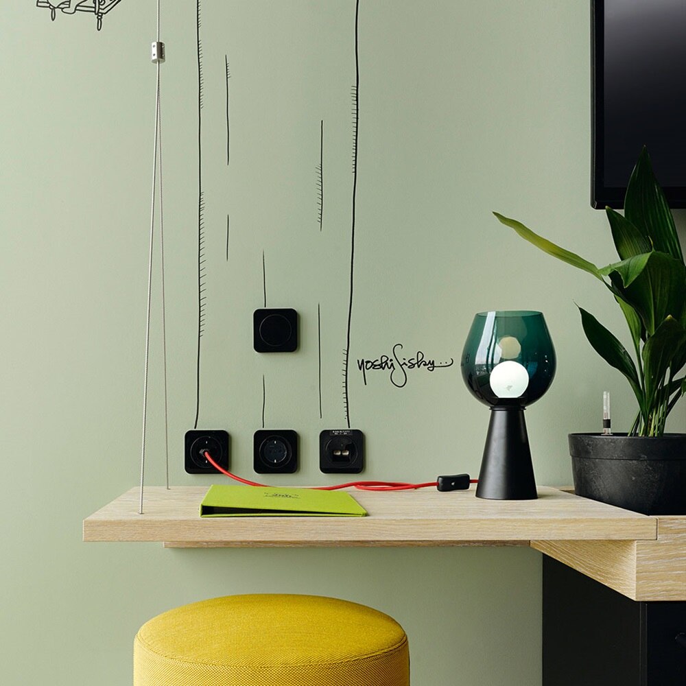 Beispiel einer Installation Berker R.1 Lichtschalter, Steckdosen und USB-Ports mit rundem Zentralstück und abgerundetem Rahmen in Schwarz auf grüner Wand mit Strichzeichnungen