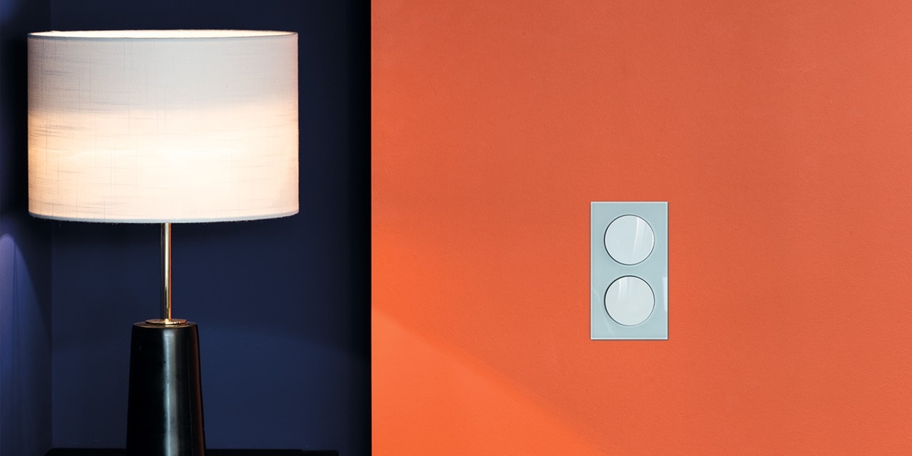 Moderne Tischlampe beleuchtet neben einer blauen Wand und ein Lichtschalter an einer kontrastierenden orangefarbenen Wand