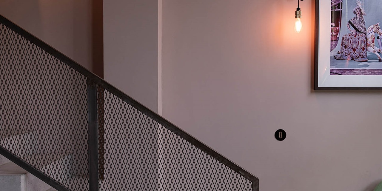Modernes Interieur mit Wandbeleuchtung und intelligentem Lichtschalter an einer rosa Wand neben einem schwarzen Treppengeländer