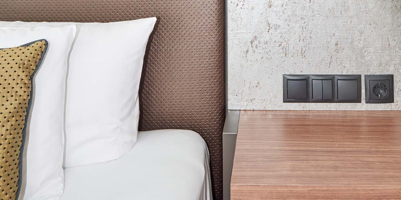 Hotelzimmer mit einer stilvollen Wand-Lichtschalterkombination und Steckdose neben dem Bett