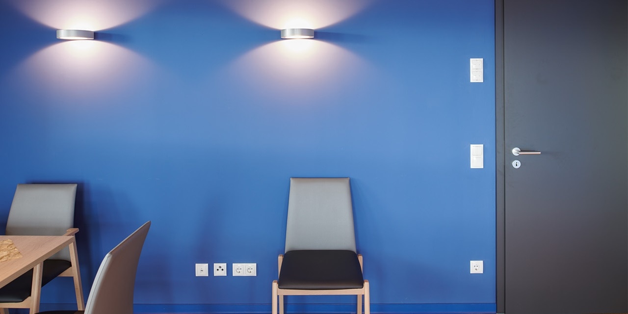 Modernes Bürointerieur mit blauen Wänden, Wandlichtschaltern, Steckdosen und Wandbeleuchtung